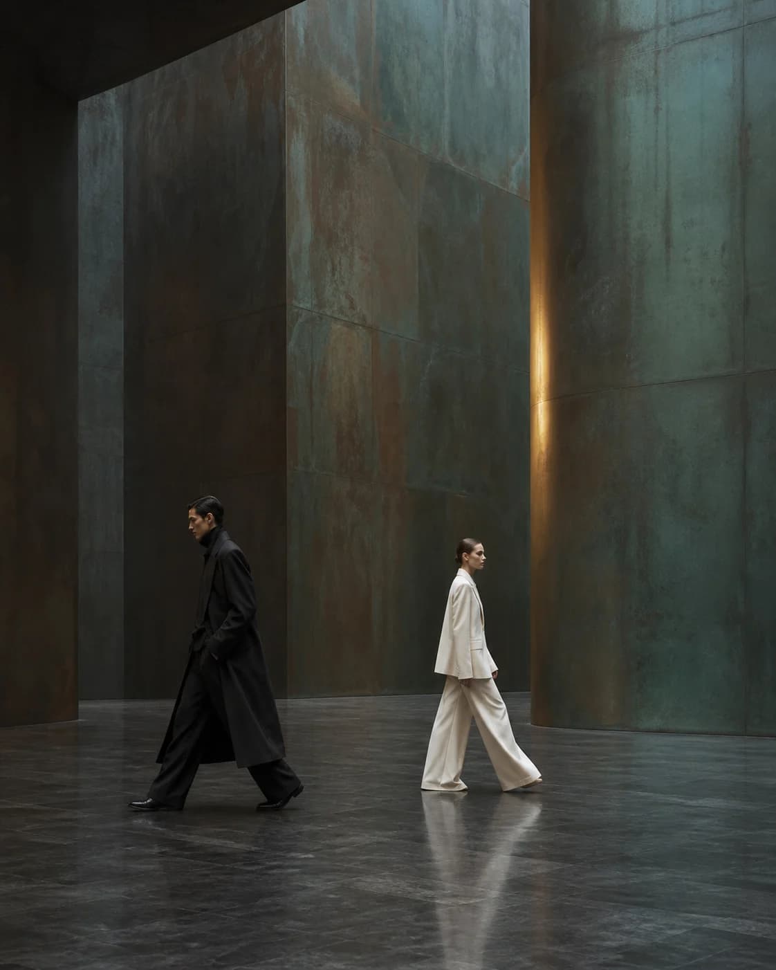 Two models in contrasting black and ivory tailoring crossing a copper gallery